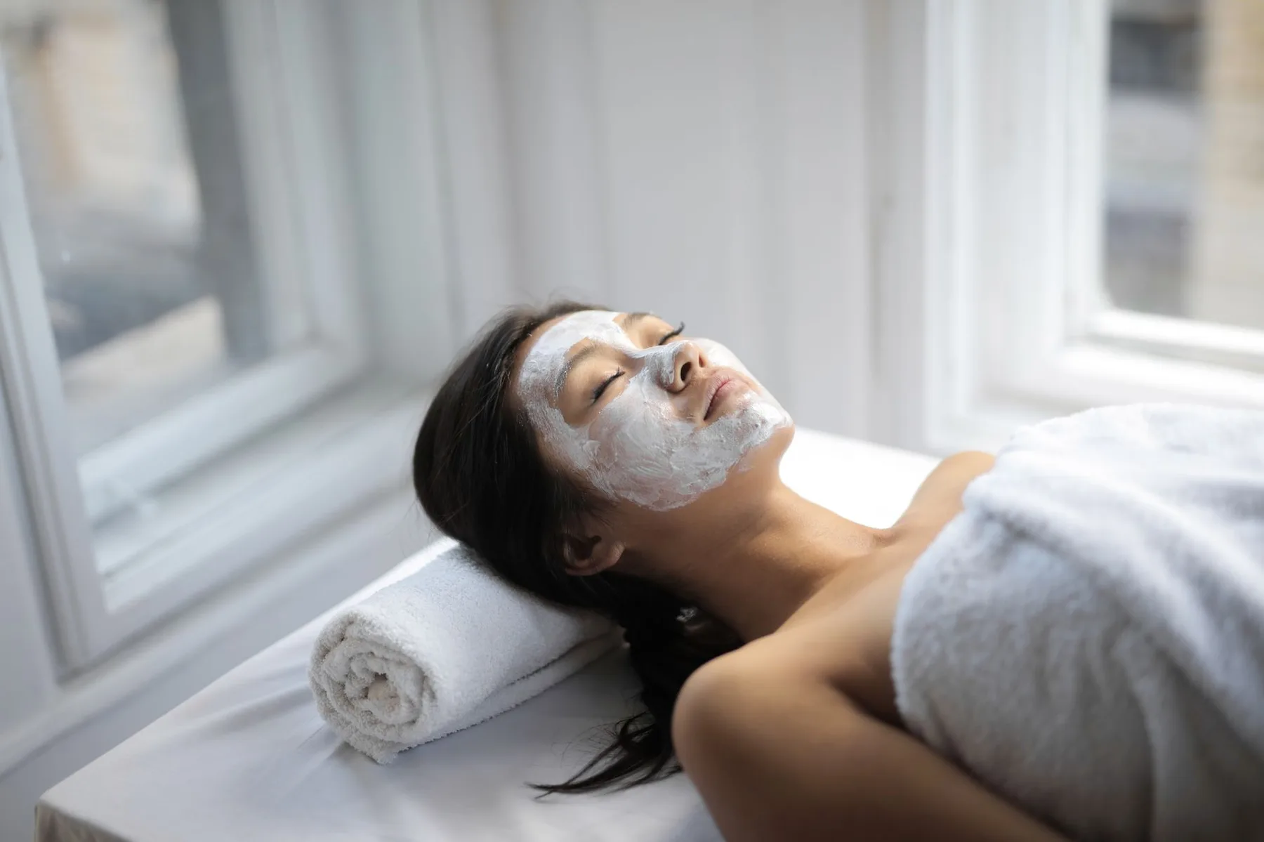 Woman relaxing with a facial mask by a bright window